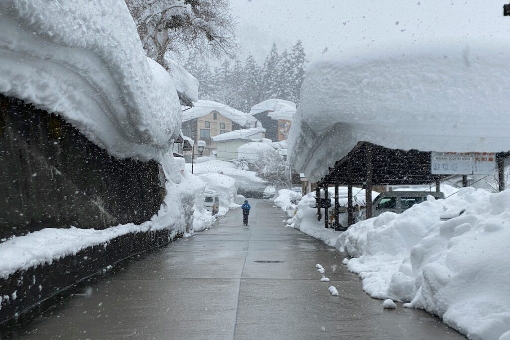 Deep snow piled on rooftops along a street in Nozawa Onsen village, Nagano, as snow falls