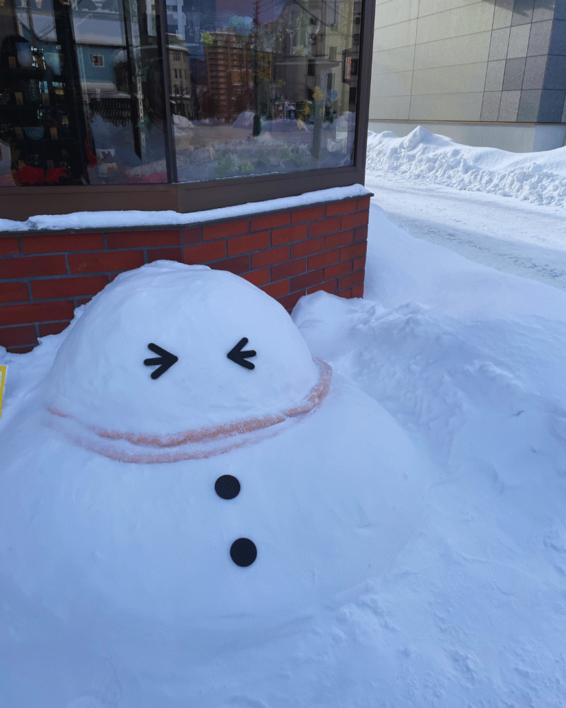 Flip Japan photo of a snowman with a scarf on the side of the street during winter in Japan