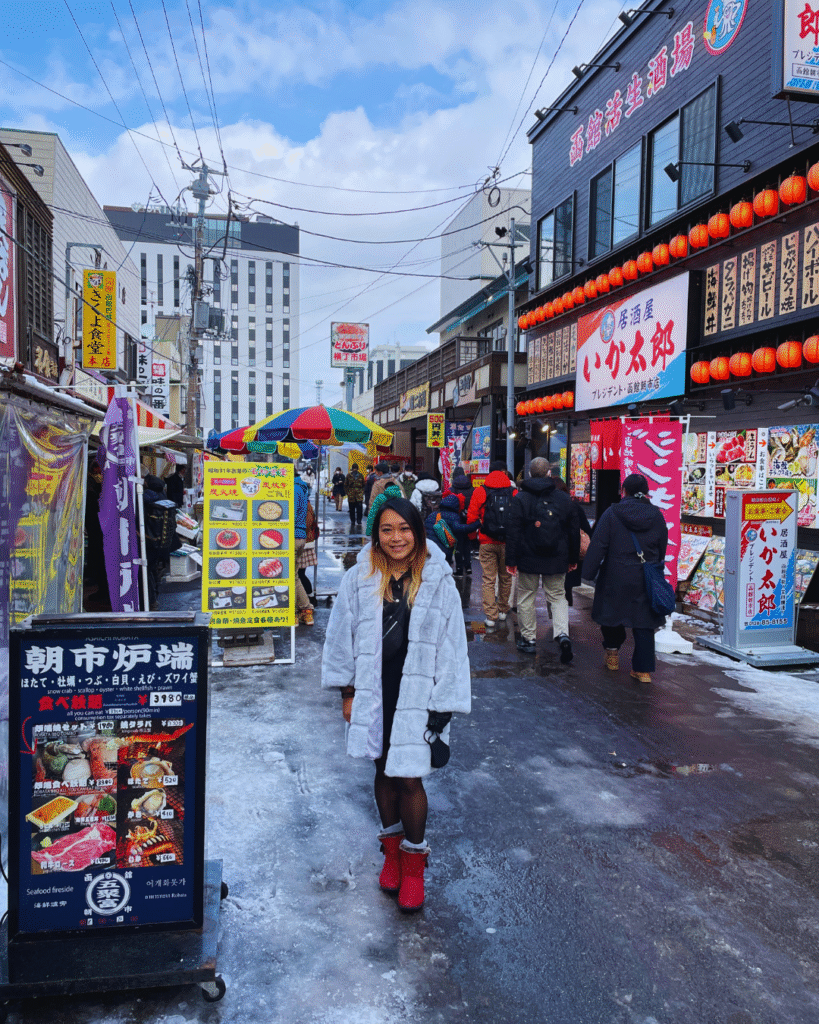 Flip Japan photo of a woman standing in a coat in a busy street of sushi restaurants during winter in Japan
