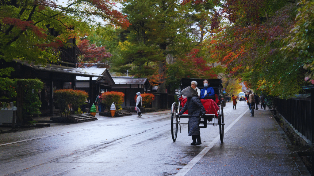 Flip Japan photo of a couple taking a rickshaw ride down a street surrounded by autumn leaves