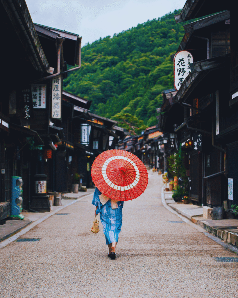 Photo of a woman with a traditional Japanese umbrella walking down an ancient postal town street