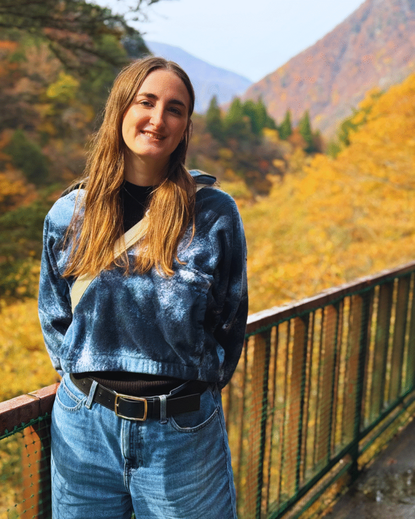 Photo of a woman standing in front of Kurobe Gorge with golden and red autumn leaves behind her