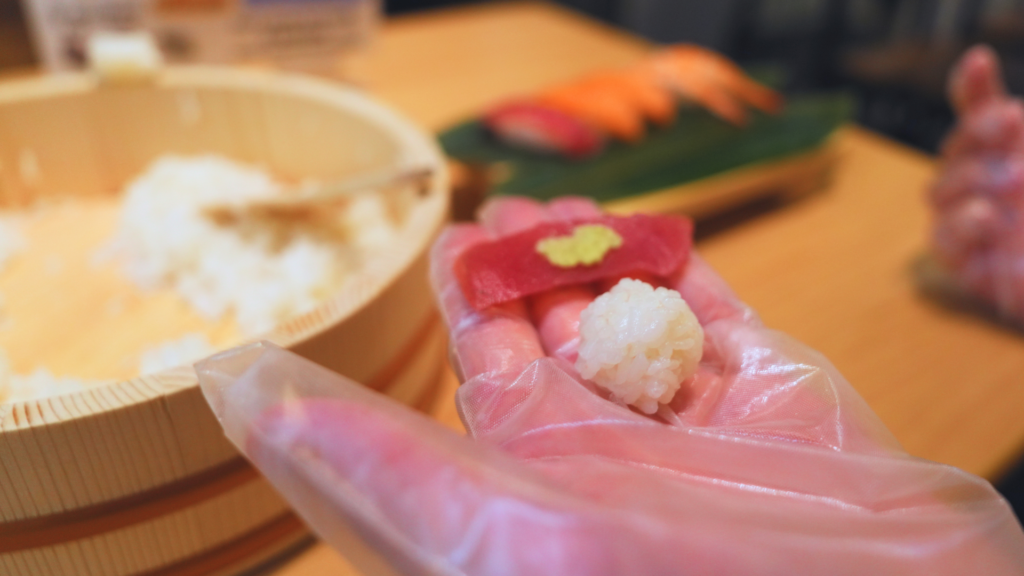 Flip Japan photo of a hand holding a small rice ball and piece of fish ready to shape into sushi