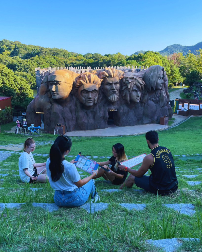 Flip Japan photo of Venese and her friends sitting in front of the Naruto stone head sculpture at Naruto Shinobi Village at Nijigen no Mori