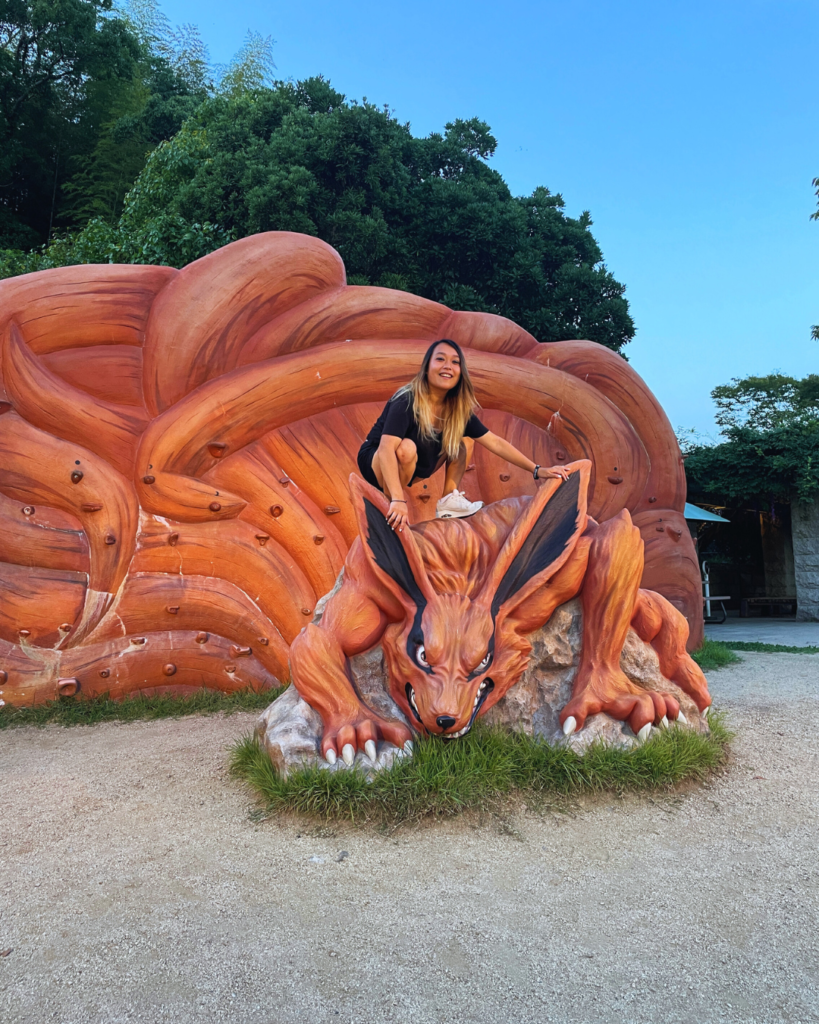 Flip Japan photo of Venese sitting on a sculpture of a fox creature in the Naruto Shinobi Village at Nijigen no Mori