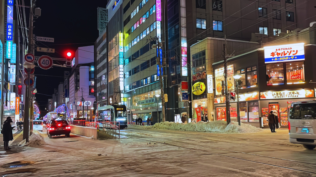 Flip Japan photo of a street in Sapporo at night with neon lights and light snow on the ground