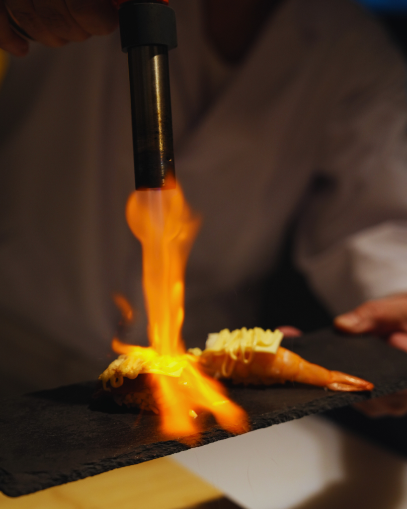 Flip Japan photo of a sushi chef using a blow torch on a piece on fish