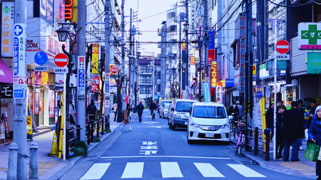 Photo of a busy street in Tokyo with shops and signs and parked cars along one side