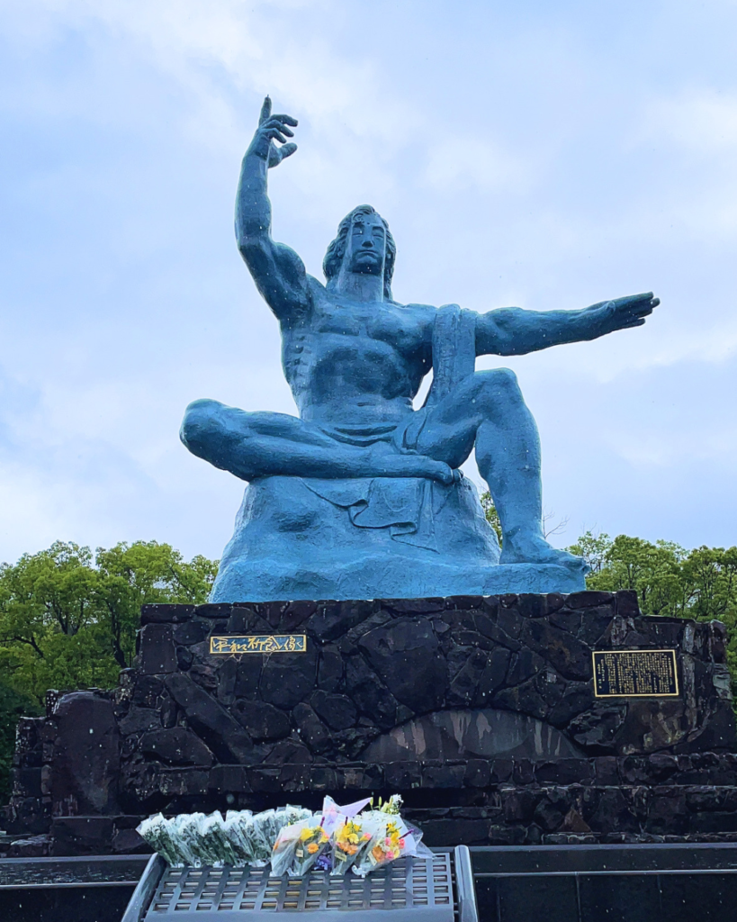 Flip Japan photo of the central statue in Nagasaki Peace Park of a man pointing to the sky with one hand and pointing to the left with the other