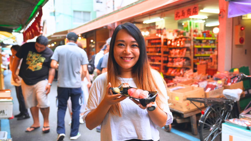 Flip Japan photo of Venese holding a plate of sushi in Tsukiji Market on day 1 of a 7-day queer japan itinerary