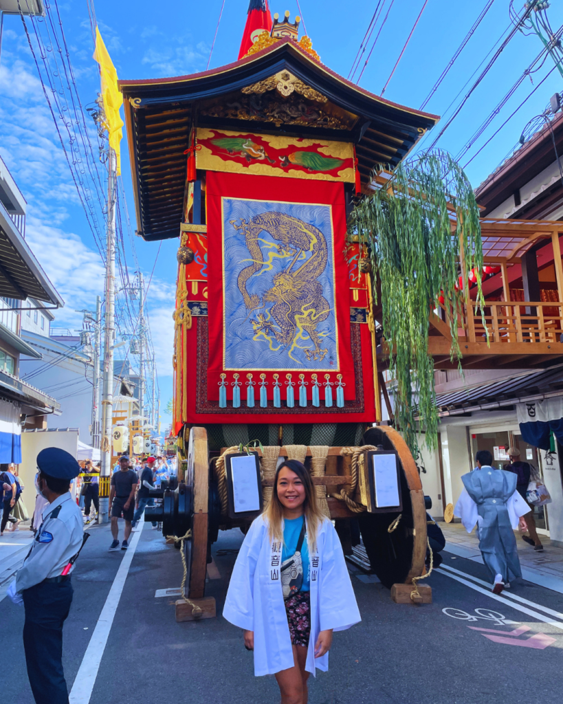 Flip Japan photo of Venese standing in front of a huge wooden float in the gin Matsuri parade