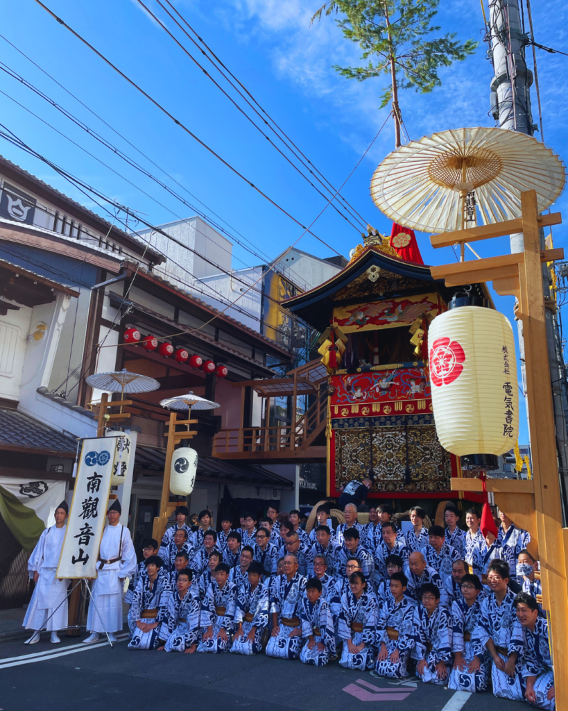 Flip Japan photo of a group of people wearing traditional yukata posing in front of a large wooden float for Gion Matsuri