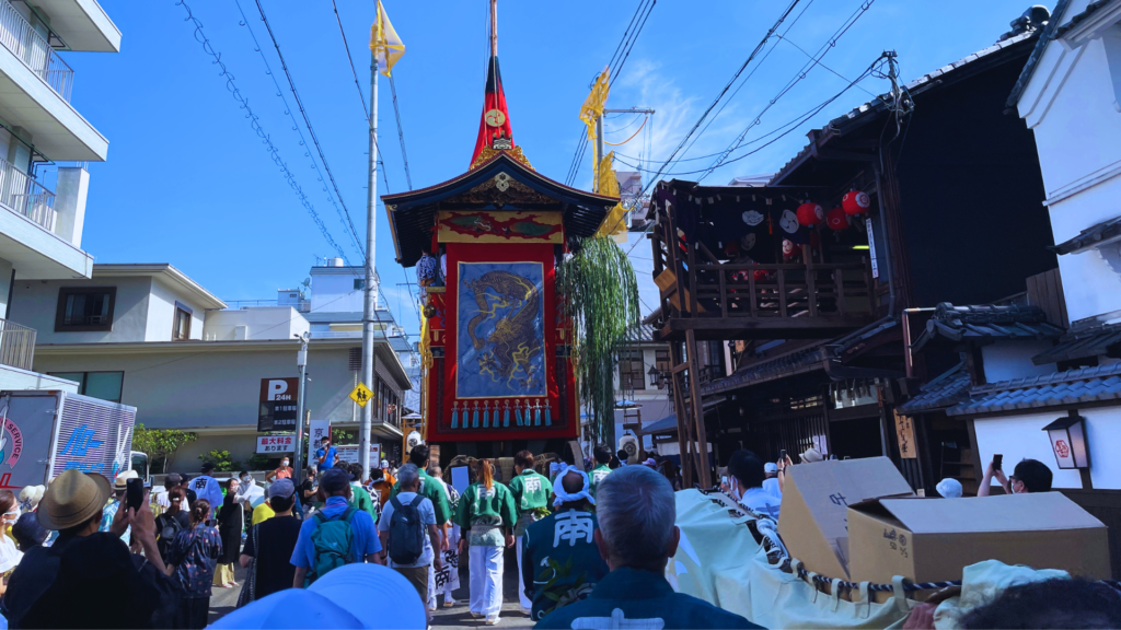 Flip Japan photo of a large wooden float followed by people wearing yukata during the Yamahoko-Junko parade in Gion Matsuri