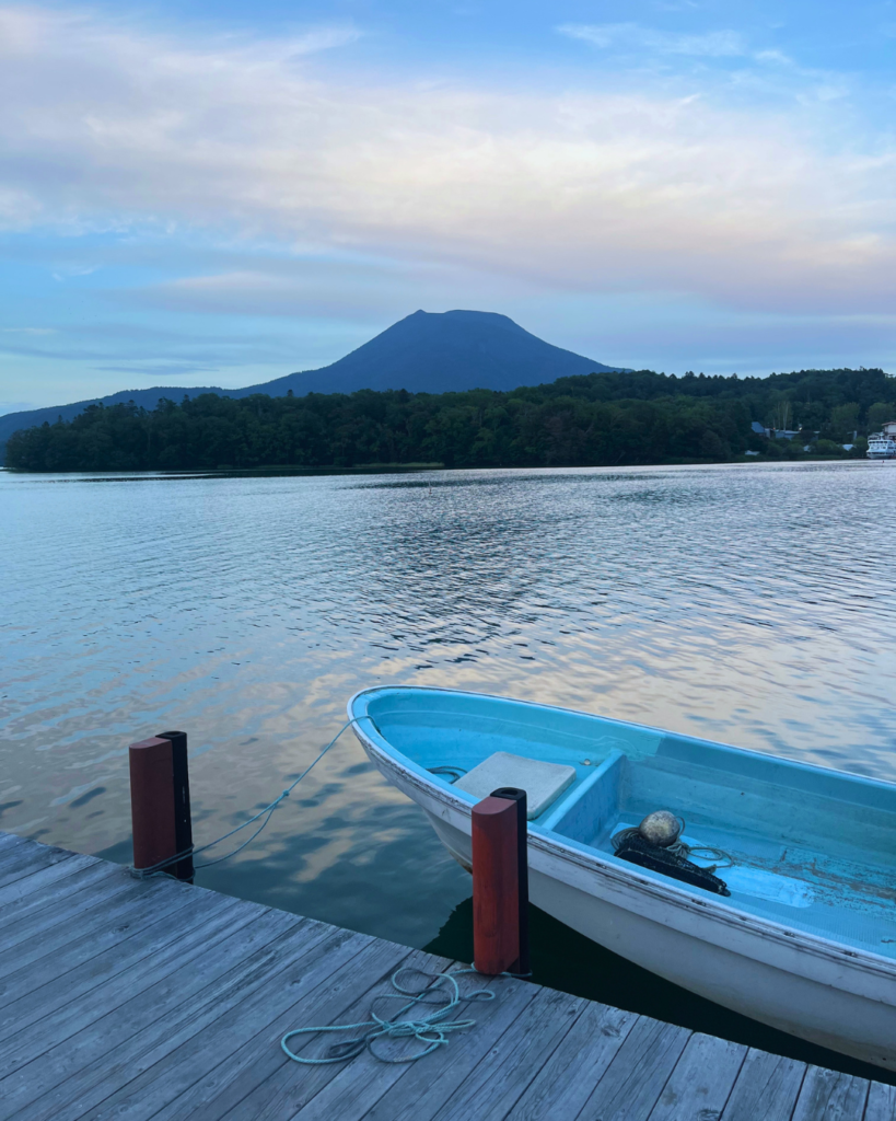 Flip Japan photo of Lake Akan with a small row boat in the foreground and a mountain in the background