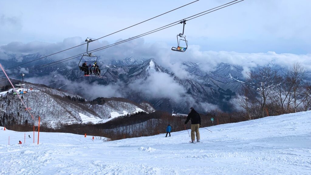 Family on a chairlift above jagged snowy mountains rising out of the clouds at GALA Yuzawa, Niigata