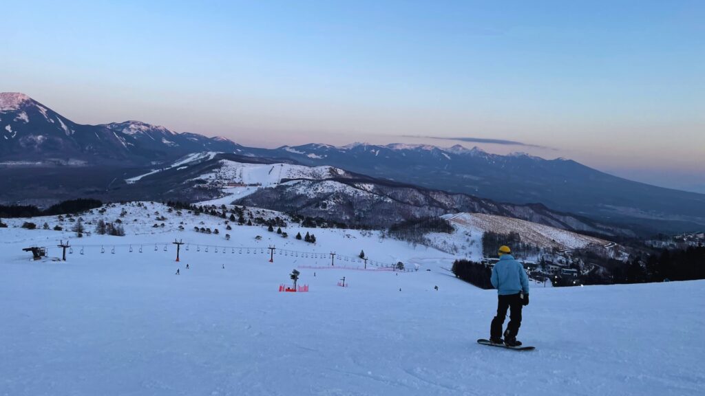 Snowboarder at dusk looking out over the slopes and pink-tinged mountain peaks at Kurumayama Kogen, Nagano, one of the closest ski resorts near Tokyo