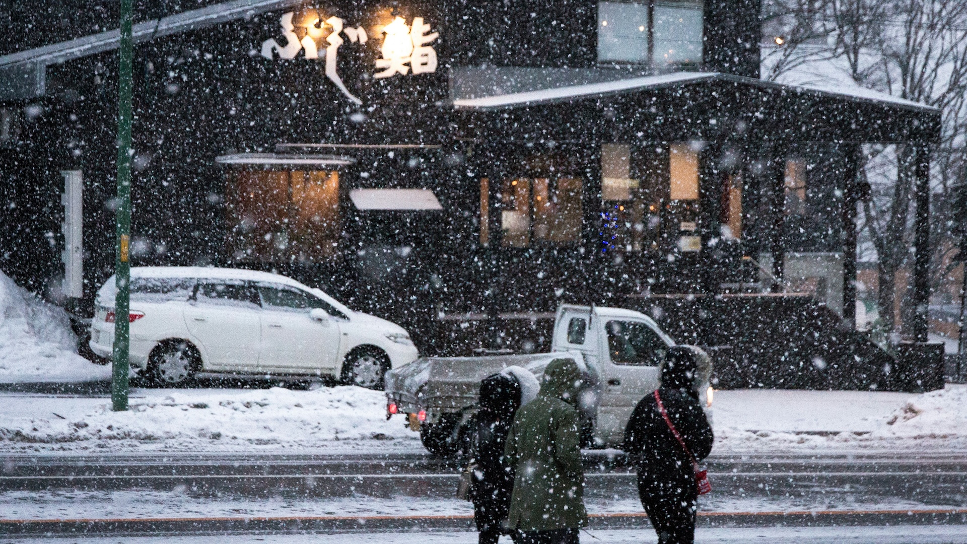 Heavy snow falling outside Fujizushi sushi restaurant as people cross the street in winter