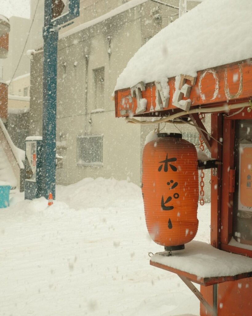 Orange paper lantern advertising Hoppy outside a bar during heavy snowfall in Sapporo